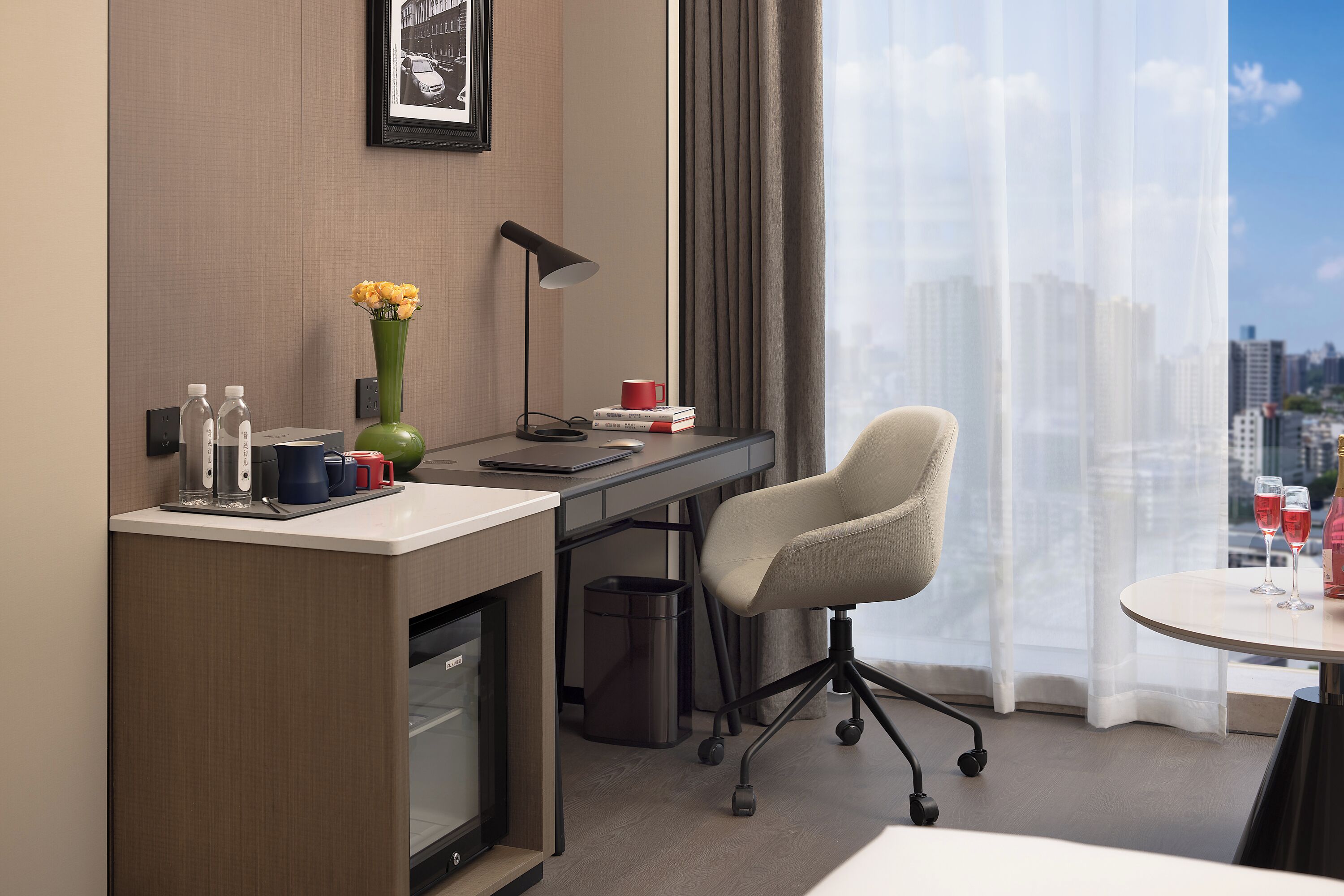 A hotel room with a desk, chair, and a view of the city.