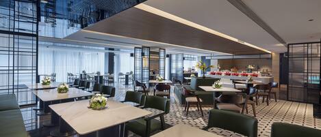 A modern dining area with tables and chairs, a kitchen area, and a seating area with a view of the city.