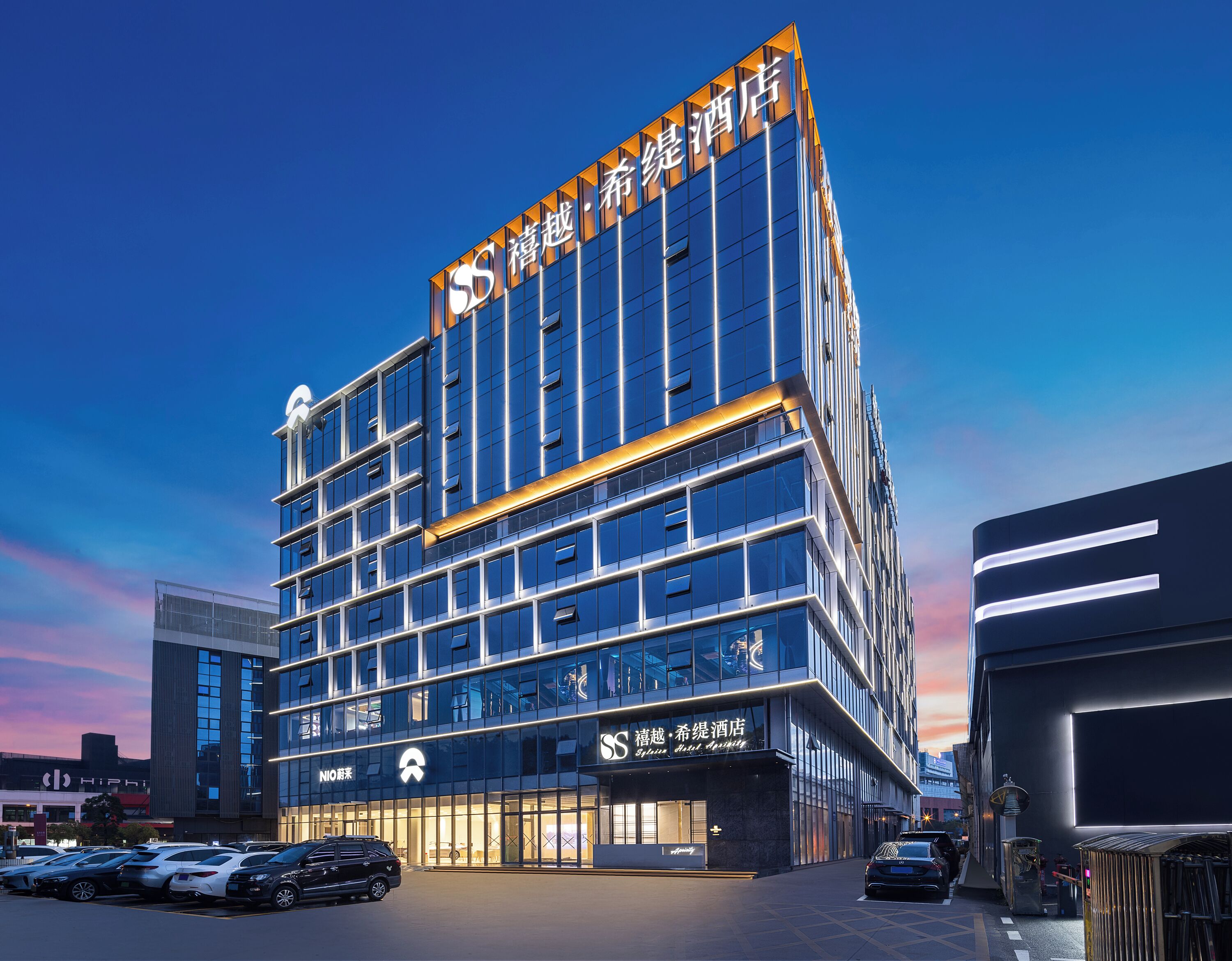 A modern hotel building with multiple floors, large windows, and a prominent sign at the top.