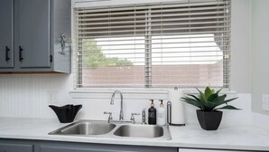 Una cocina con un lavamanos doble, una ventana con persianas, una planta en maceta y un lavavajillas.