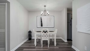 Un comedor con una mesa y sillas blancas, una araña y una obra de arte enmarcada en la pared.