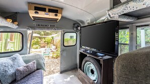 A van interior with a sofa, pillows, a television, and an emergency door. - Cozy 3BR Retreat - Near Bars, Zoo & Lake Trails (Sanford)