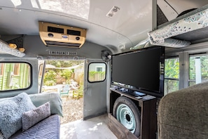 A van interior with a sofa, pillows, a television, and an emergency door.