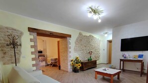 Un salón con un sofá blanco, una mesa de centro, un televisor y una pared de piedra.