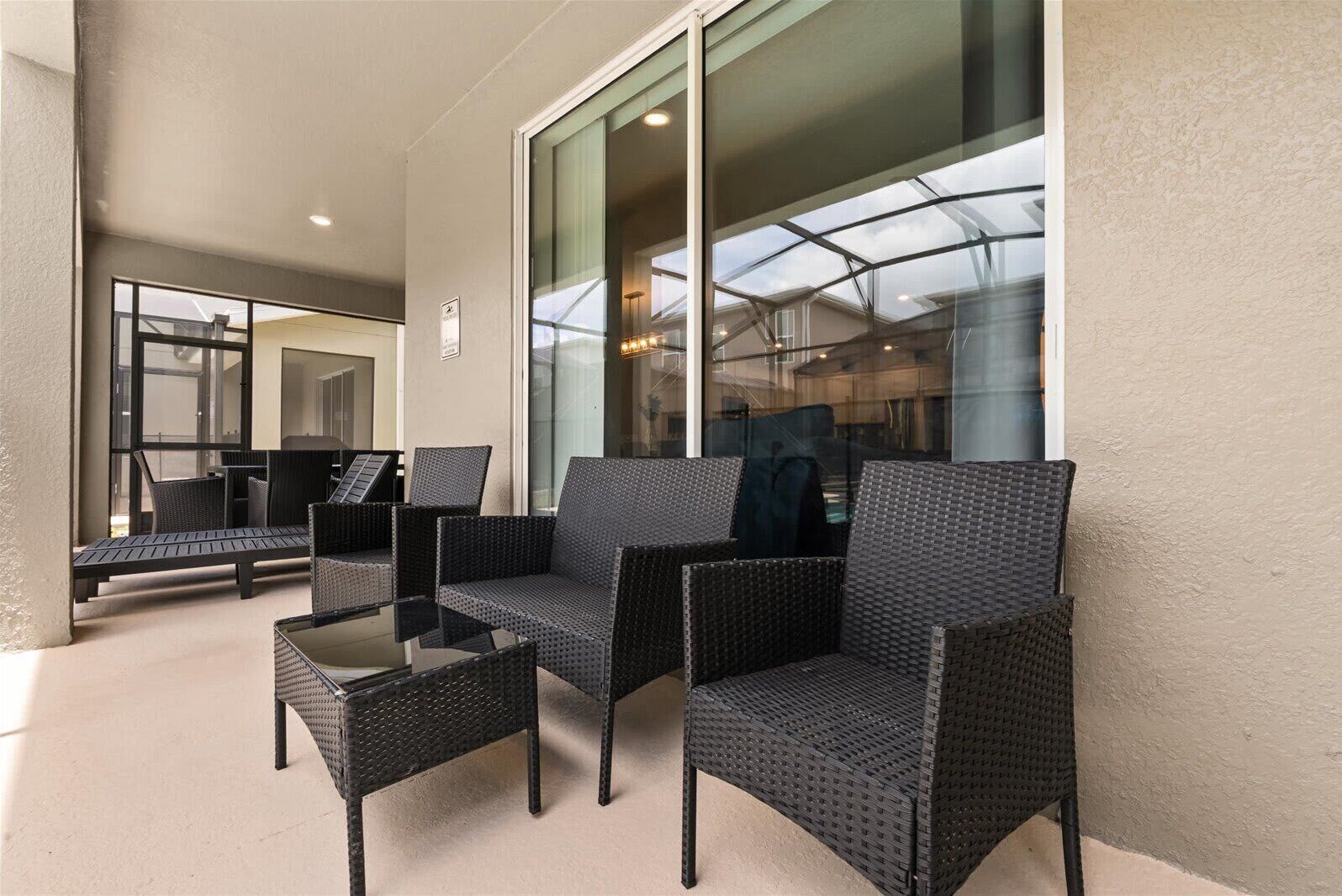 A covered outdoor seating area with wicker furniture and a glass wall.