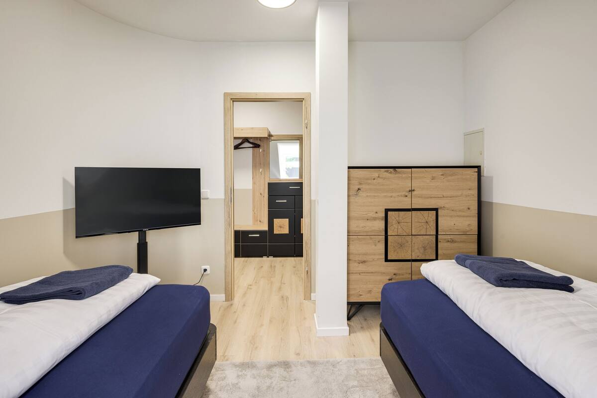 A modern hotel room with two beds, a TV, a wooden wardrobe, and a walk-in closet.