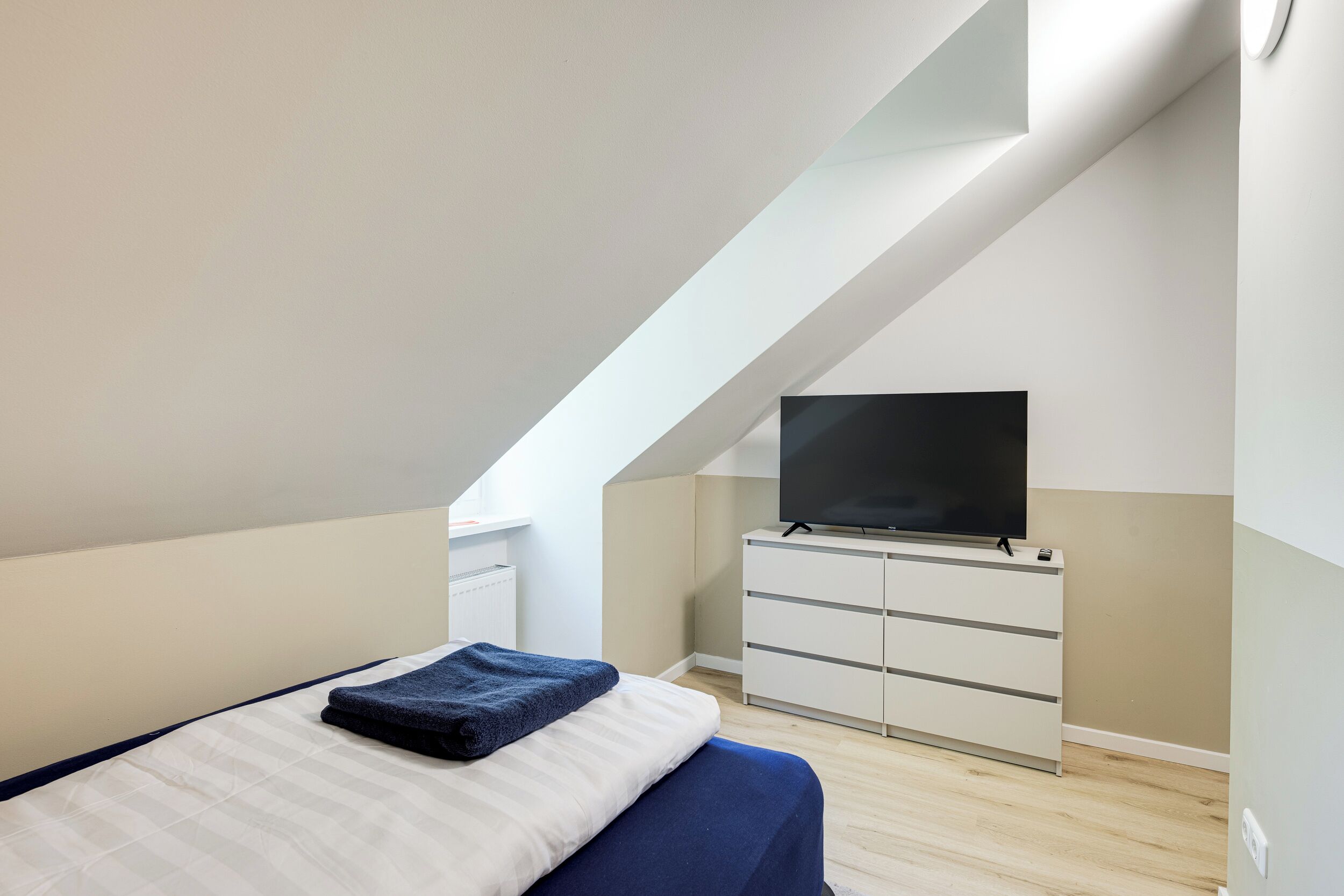 Un dormitorio moderno con cama, televisor de pantalla plana y cómoda blanca.