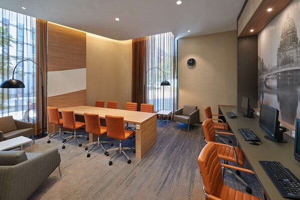 A modern meeting room with a large table, conference chairs, a sofa, and a computer setup.