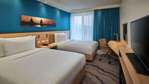 Een hotelkamer met twee bedden, een bureau, een stoel, een televisie en een schilderij aan de muur.