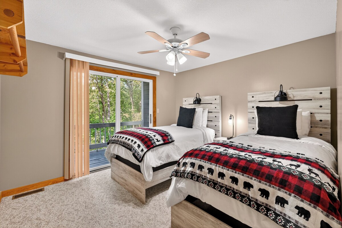 A bedroom with two beds, a ceiling fan, a large window, and a wooden headboard.