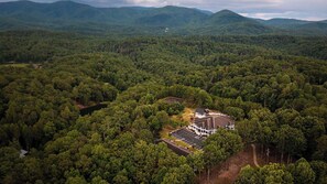 An aerial view of a forested area with a building featuring a parking lot and a large structure with a sloped roof. - The Ellijay Resort (Ellijay)