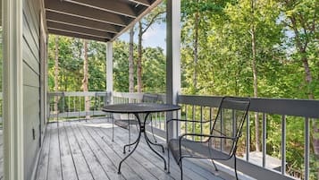 A wooden deck with a table and chairs, surrounded by a railing, overlooking a forested area.