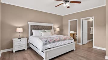 A bedroom with a bed, nightstands, a ceiling fan, and a door leading to another room.