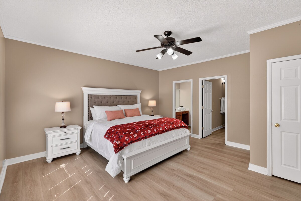 A bedroom with a bed, nightstands, a ceiling fan, and a door leading to another room.