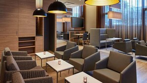 Een moderne hotellobby met zitgedeeltes, een televisie en grote ramen.