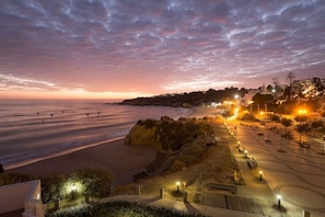A coastal view with a beach, a staircase leading down to the beach, and a lit pathway. - Unwind and Rejuvenate! Beachfront Flats w/ Balcony in Iconic Landmark (Albufeira)