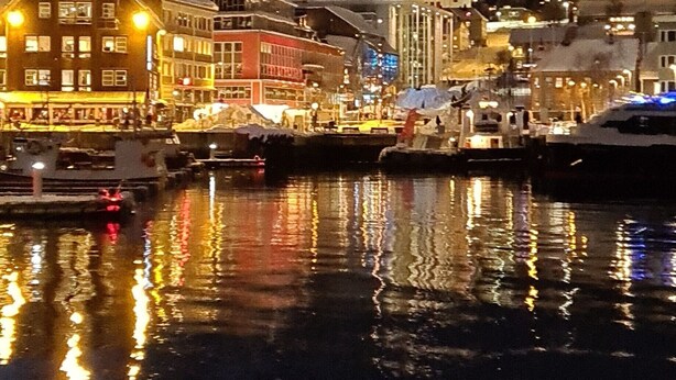 A waterfront marina at night with illuminated buildings reflecting on the water.