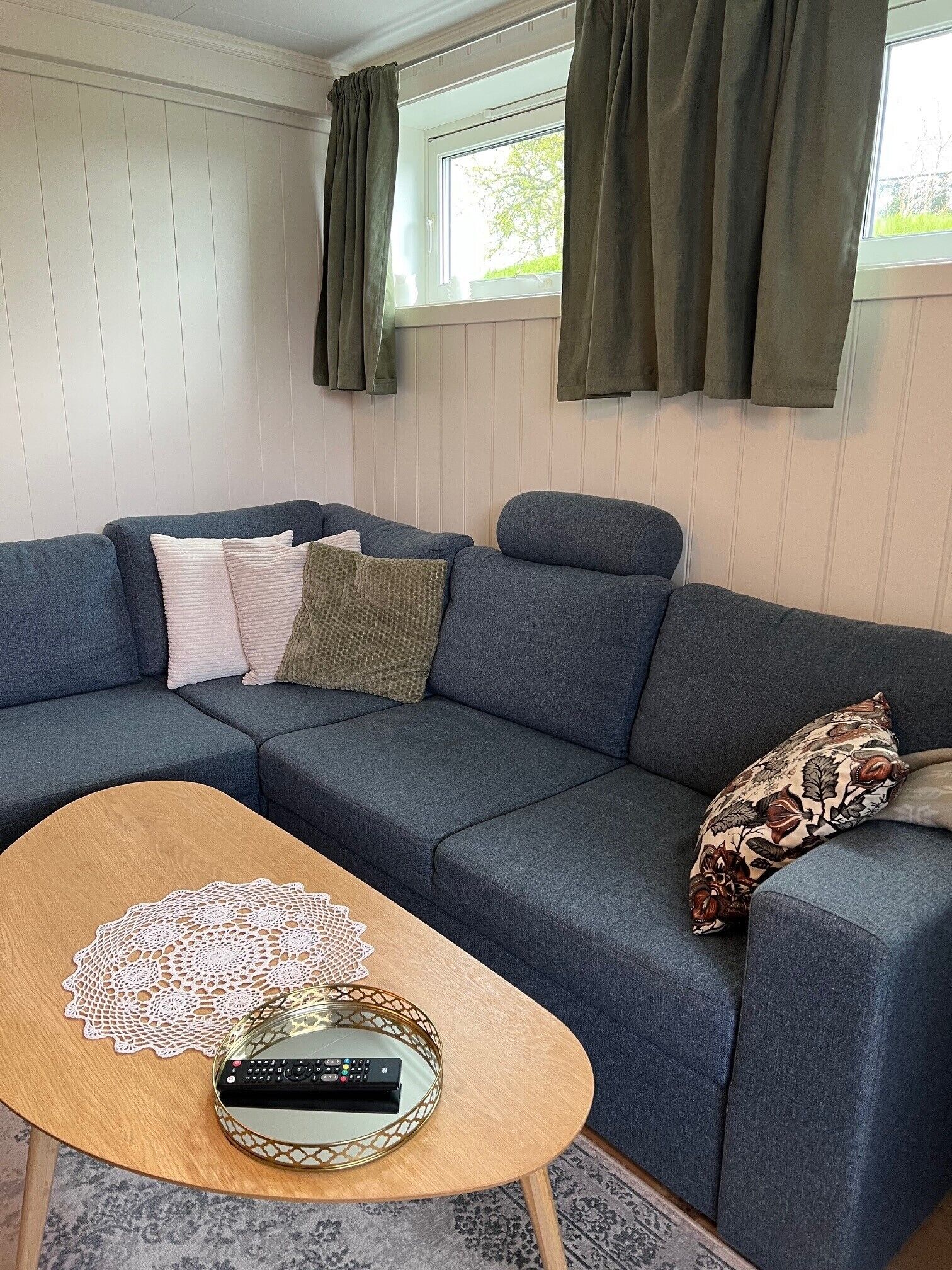 Una sala de estar con un sofá modular, una mesa de centro de madera y una ventana con cortinas.
