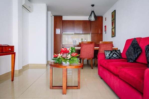 A modern living room with a red sofa, a wooden coffee table with flowers, and a kitchen in the background.
