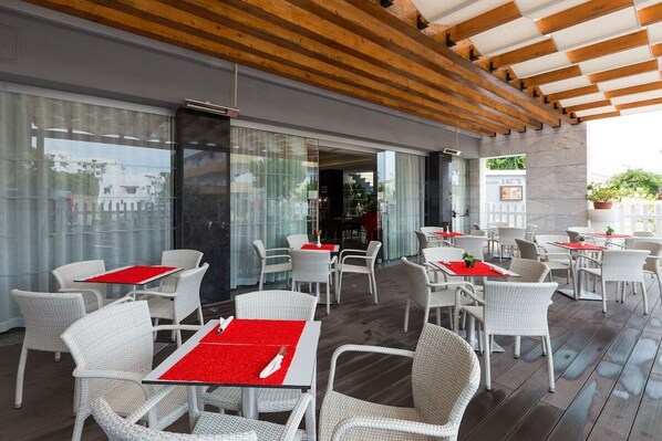 Un espace de restauration extérieur moderne, avec des chaises et des tables en osier blanc, certaines agrémentées de sets de table rouges.