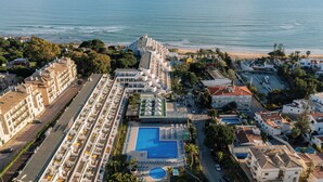 An aerial view of a resort with a large pool, multiple buildings, and a beach in the background.