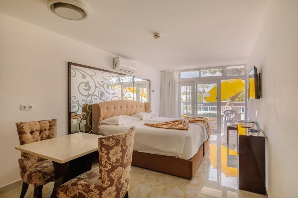 A hotel room with a bed, a dining table, and chairs. There is a balcony with a yellow umbrella.