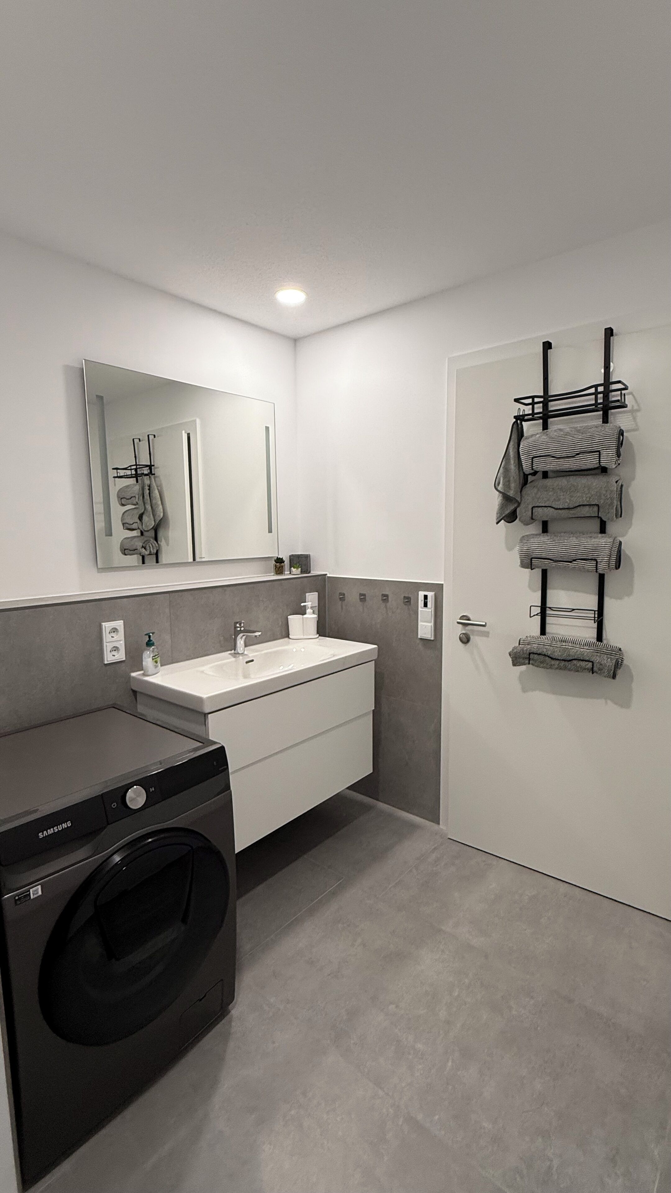 Une salle de bain moderne équipée d’un lave-linge intégré, d’un lavabo et d’un porte-serviettes.