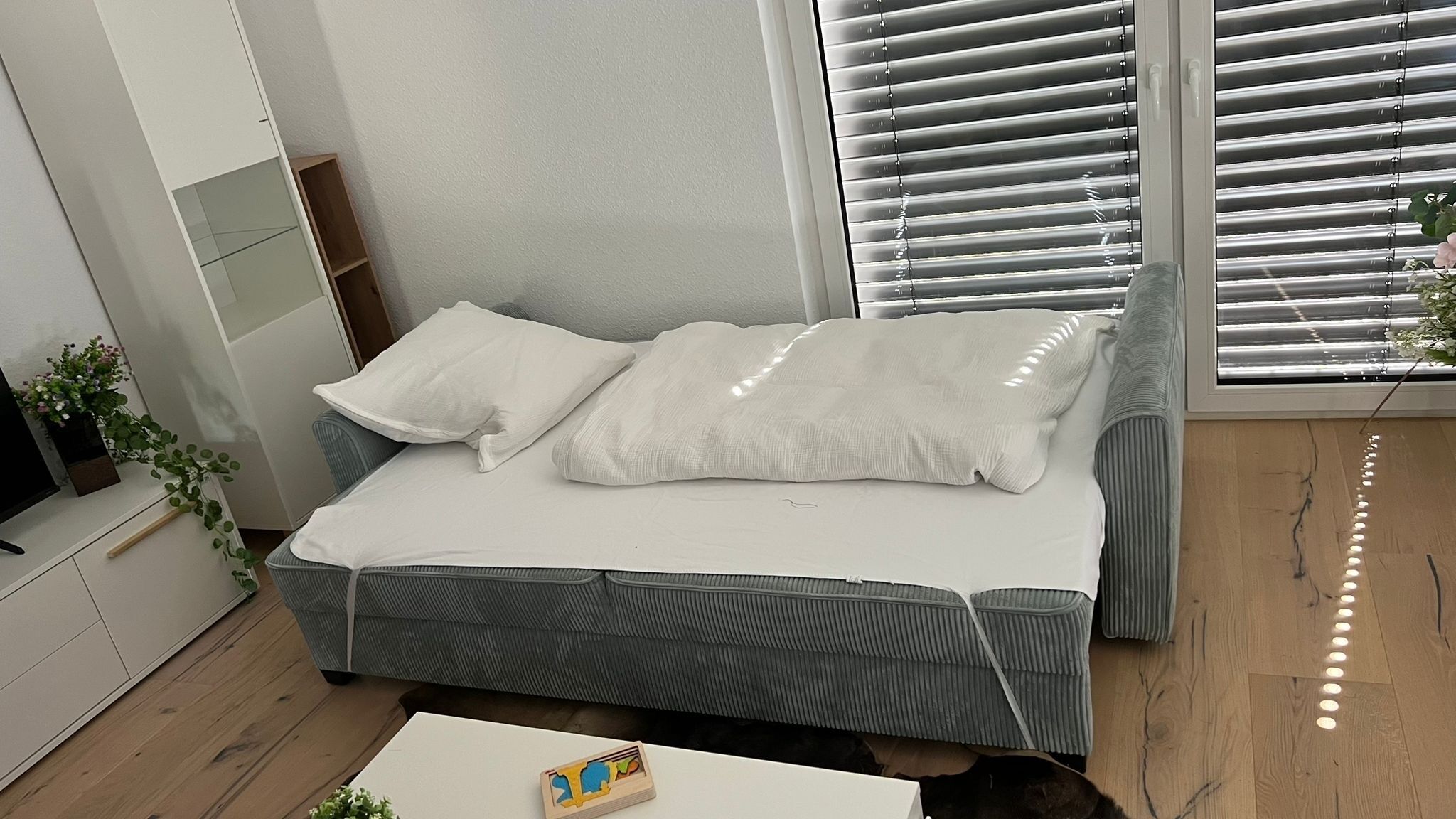 Un dormitorio moderno con cama, una mesita y una ventana con persianas.