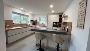 A modern kitchen with a central island, bar stools, and a view of greenery outside. - Vacation apartment at the Teufelsloch in the Ahr valley not far from the Nürburgring (Altenahr)