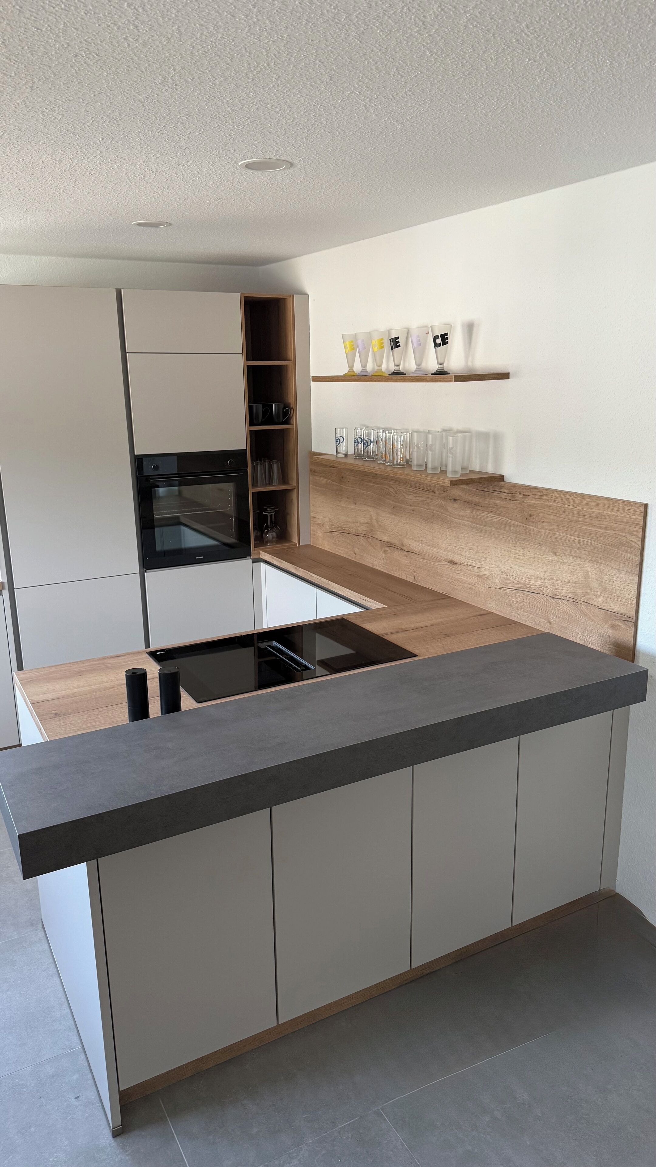 Une cuisine moderne dotée d’un îlot central, d’un four encastré et d’étagères en bois.