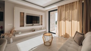 A modern living room with a flat-screen TV mounted on the wall, a round wooden coffee table, and a beige sofa.