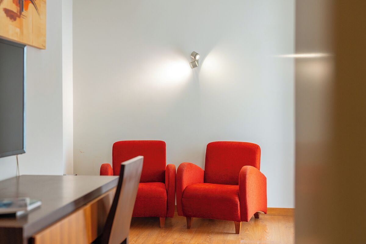 A room with two red chairs, a wooden desk, and a wall-mounted light fixture.