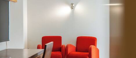 A room with two red chairs, a wooden desk, and a wall-mounted light fixture.
