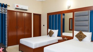 Habitación de hotel con dos camas, un armario, aire acondicionado, escritorio con silla y ventilador de techo.