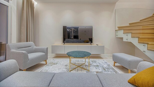Una sala de estar moderna con un juego de sofá, una mesa de centro redonda y un televisor sobre un mueble blanco.