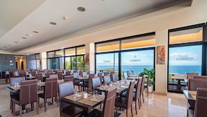 Un ristorante spazioso con numerosi tavoli e sedie, ampie finestre con vista sul mare e un design d'interni moderno.