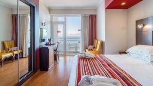 A hotel room with a bed, a desk, a chair, a mirror, and a view of the sea. - Explore Funchal's Marina! Balcony with Sea View, Swimming Pool, Spa & Wellness! (Funchal)