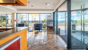 A modern hotel lobby with a reception desk, seating area, and large windows offering a view of the ocean. - Budget-Friendly Stay in Madeira Island! Outdoor Pool, Spa Center, Beachfront! (Funchal)