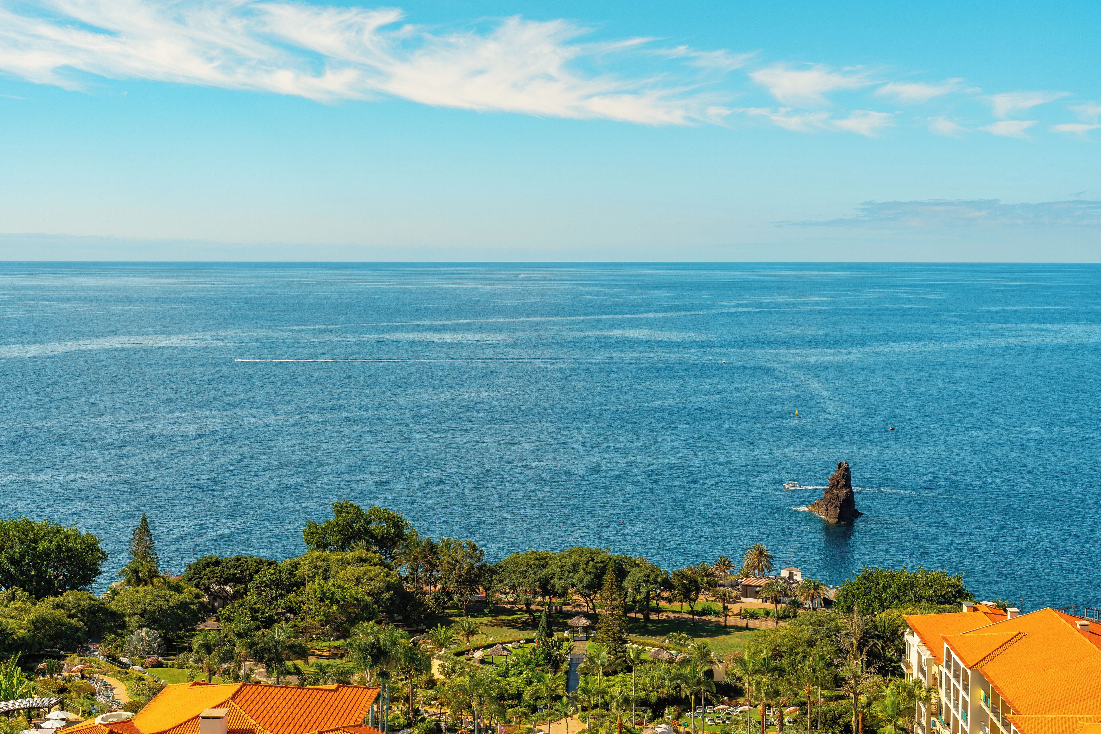 A coastal view with a rocky outcrop in the sea, surrounded by greenery and buildings with orange roofs.