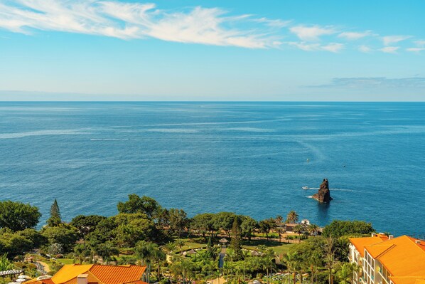 Une vue côtière avec un promontoire rocheux dans la mer, entouré de verdure et de bâtiments aux toits orange.