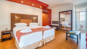 A hotel room with two beds, a wooden headboard, a red accent wall, a large mirror, and a balcony with a view.