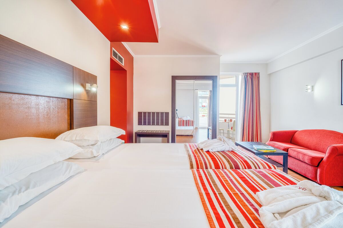 A hotel room with two beds, a red sofa, a striped rug, and a view of the outside.