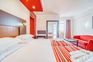 A hotel room with two beds, a red sofa, a striped rug, and a view of the outside. - Stay Close to Lido Promenade! Balcony with Sea View, Breakfast, Pool! (Funchal)