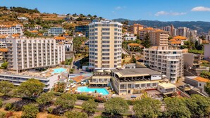 A hotel with multiple floors, a swimming pool, and a view of the surrounding hills. - Ultimate Madeira Getaway! Garden View, Swimming Pool, Close to Lido Promenade (Funchal)