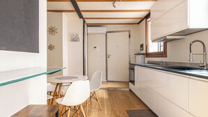 A compact kitchen with white cabinets, a wooden dining table, and a white chair. - Basilica Prestige 5* Residence, luxury and comfort (Vicenza)