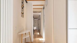 A narrow hallway with a white chair and a small table, wooden beams on the ceiling, and a door at the end. - Basilica Prestige 5* Residence, luxury and comfort (Vicenza)