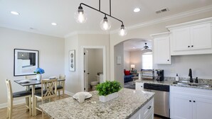 A modern kitchen with white cabinets, granite countertops, and a dining area with a table and chairs. - "Swayze Stays" - Charming Oxford Condo! (Oxford)