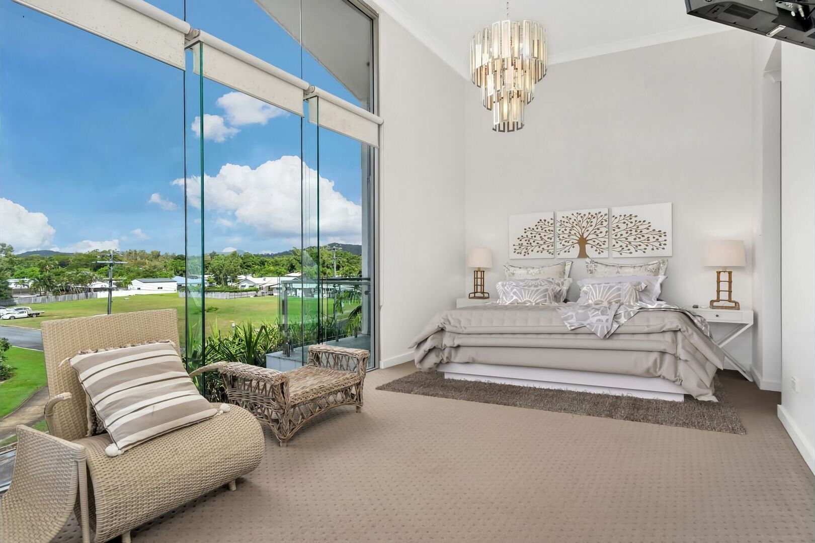 A bedroom with a large window, a bed, a chandelier, and a view of a green landscape.