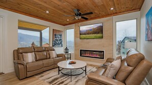 A modern living room with a fireplace, leather sofas, a coffee table, and a large TV. - 🏔️ Apres All Day 🌙 Rooftop Mountain Views, Putting Green, Hot Tub & Arcade (Gatlinburg)