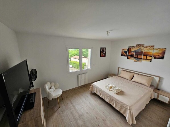 Une chambre à coucher avec un lit, une télévision, une chaise, une fenêtre et des œuvres d’art accrochées au mur.